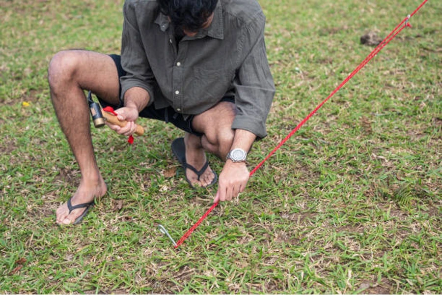 Homme utilisant un petit maillet de camping pour fixer la corde de la tente