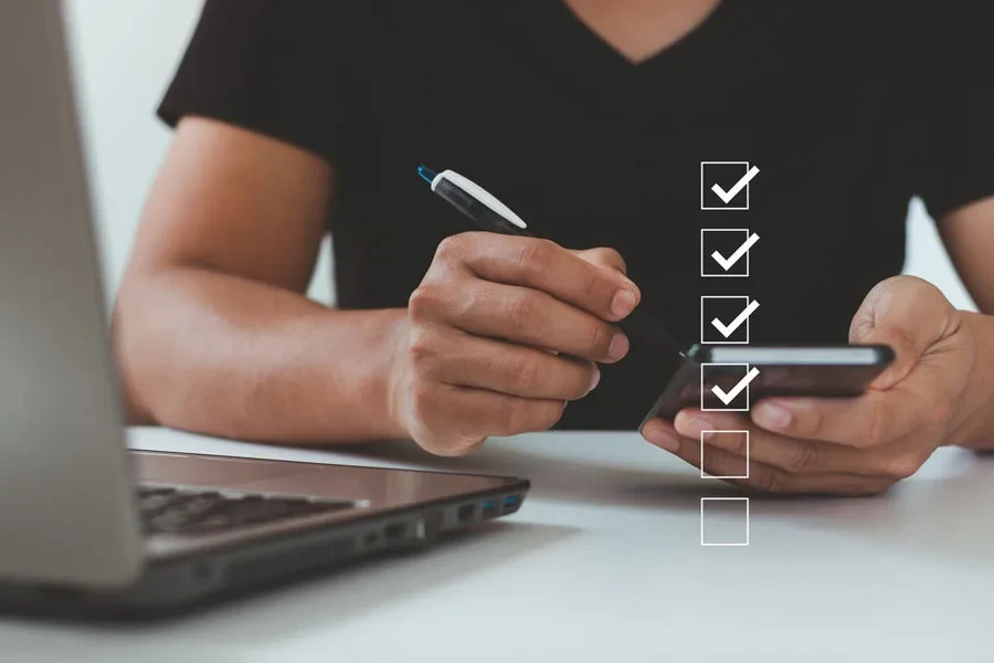 Hombre usando teléfono y computadora portátil, marcando la lista