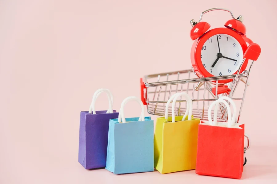 Sacolas de compras multicoloridas e despertador em fundo rosa