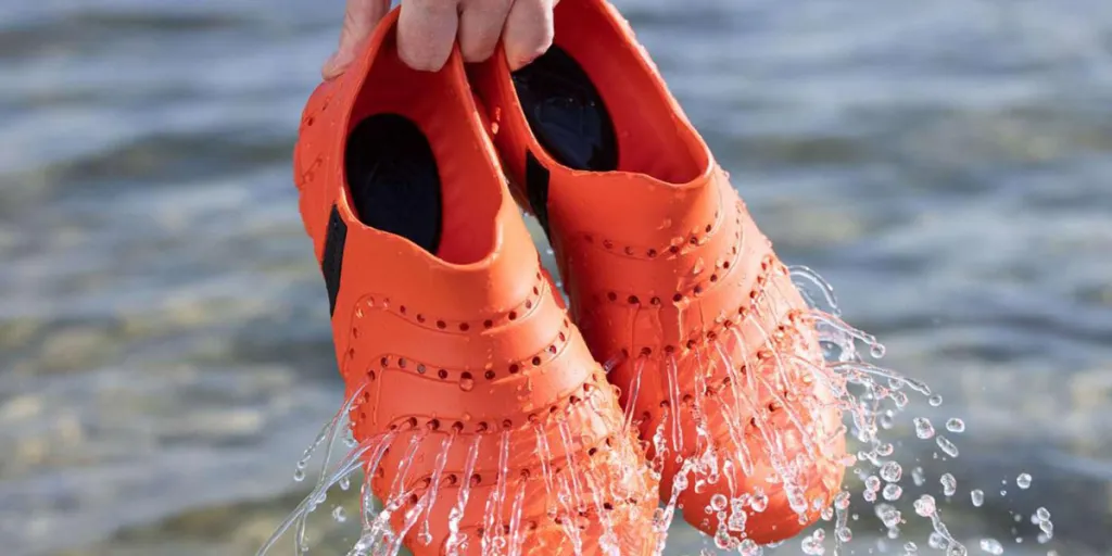 Pessoa segurando um par de botas de água laranja
