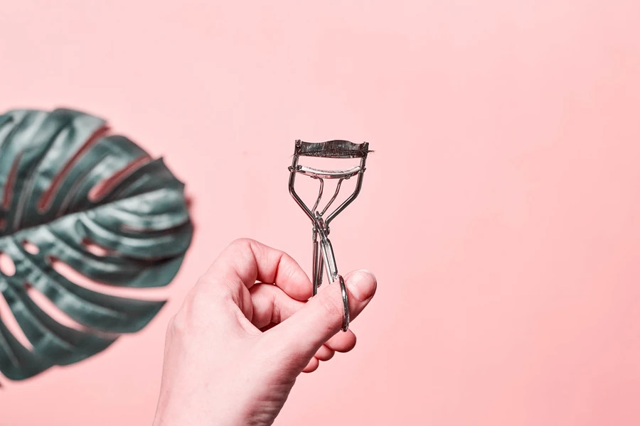 Person holding an eyelash curler on a pink background