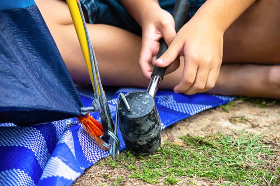 Person using rubber camping mallet to pull up steel peg