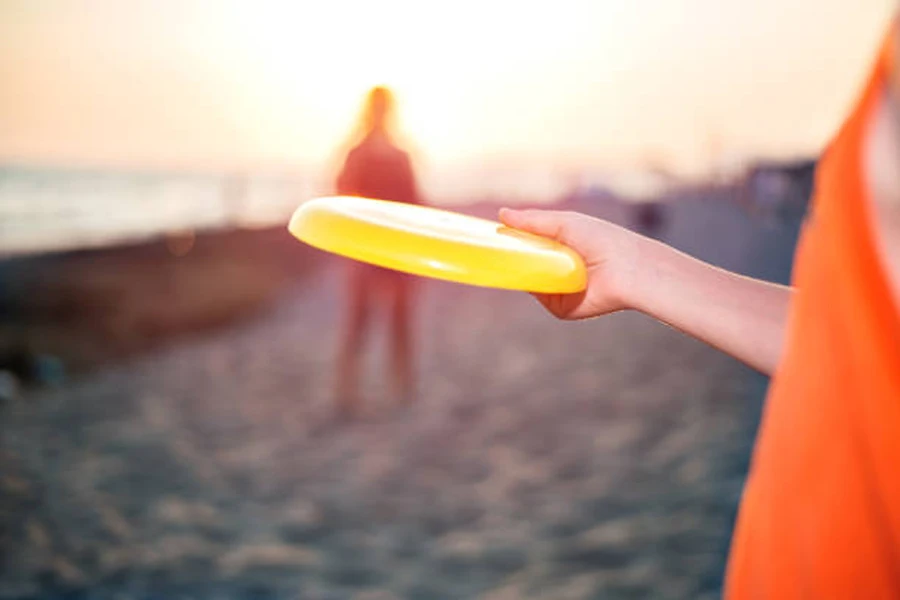 Persona vestida de naranja sosteniendo un frisbee amarillo en la playa al atardecer