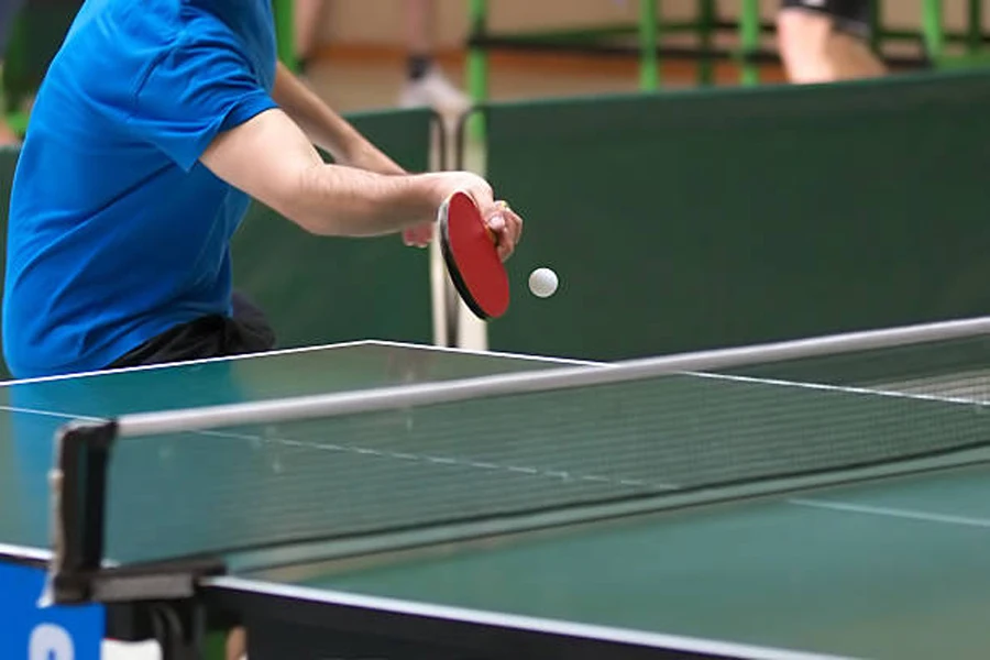 Masa tenisi masasının ağ üzerinden topa vuran oyuncu