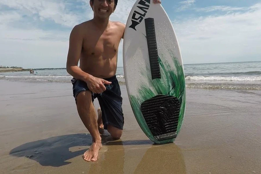 Smiling man posing next to skimboard