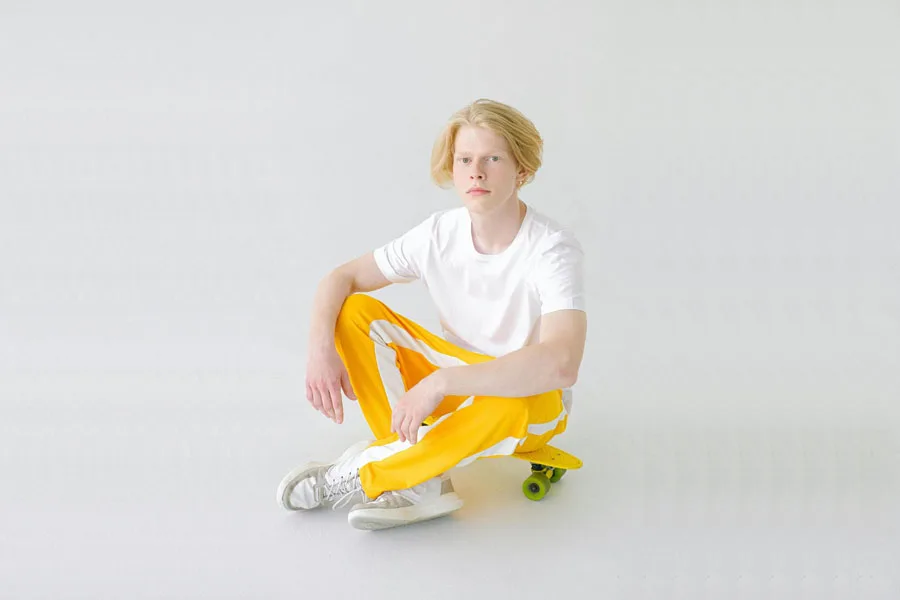 Teenager in bright yellow trousers resting on skateboard