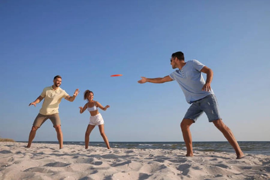 Tiga orang melempar frisbee merah di sekitar pantai