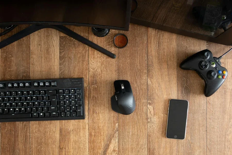 Vue de dessus d'une manette de jeu noire avec souris et clavier sur un bureau en bois avec moniteur