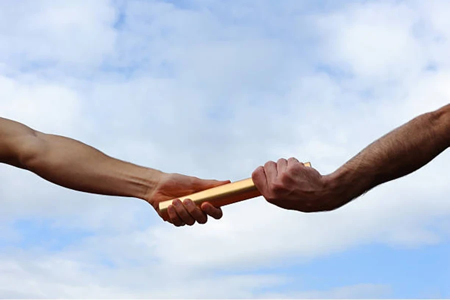 Two hands passing a golden metal relay baton between them