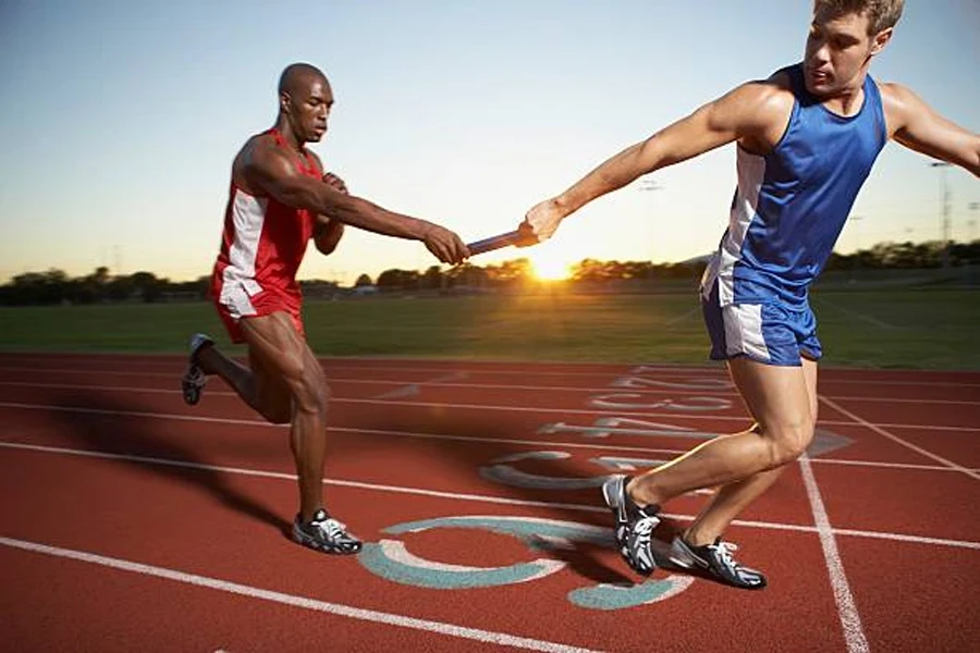 Dois homens passando bastão de revezamento entre eles na pista