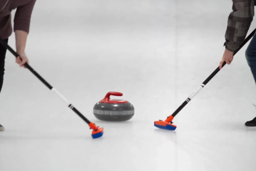 Due spazzatrici sulla pista di pattinaggio spazzano la pietra da curling con manico rosso