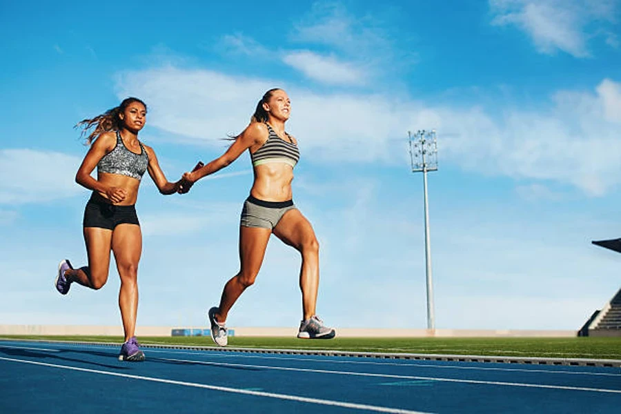 Two women running on track passing relay baton between them