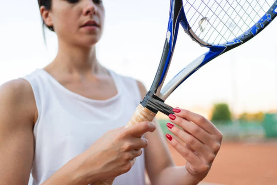 Frau korrigiert Klebeband am Ende des Tennisschlägergriffs