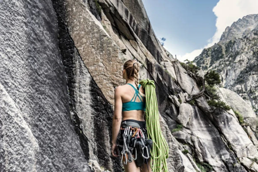 Donna che tiene la corda e diversi moschettoni alla base della roccia