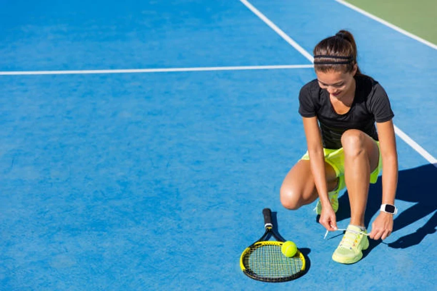 Wanita mengikat sepatu tenis ringan di lapangan keras biru