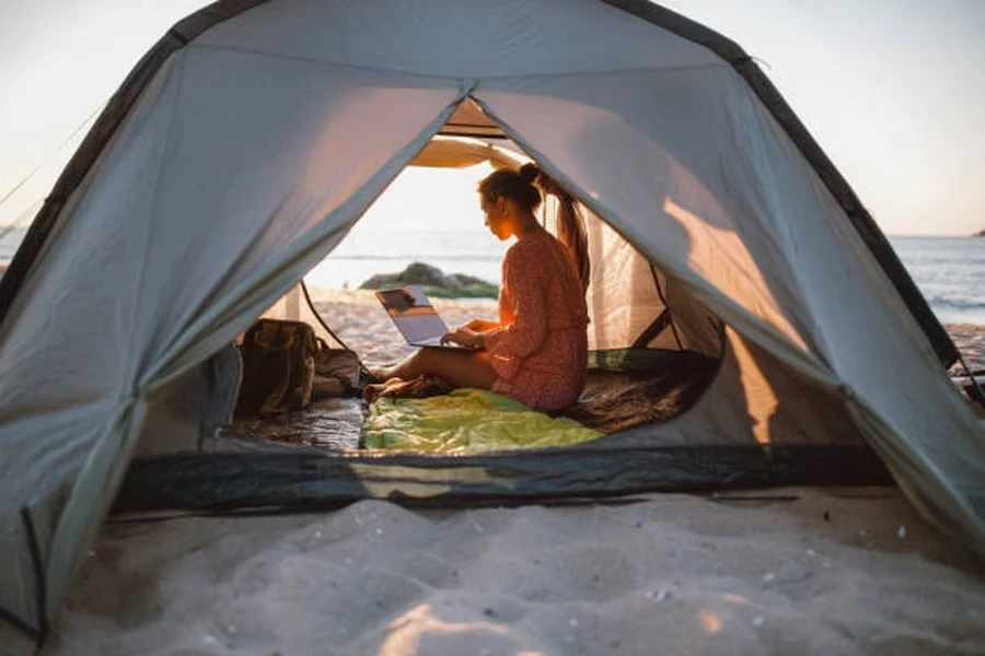 Mulher sentada dentro de uma barraca de praia pop-up com laptop