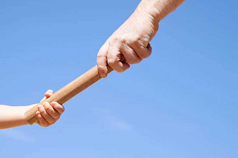 Wooden relay baton being transferred between two hands