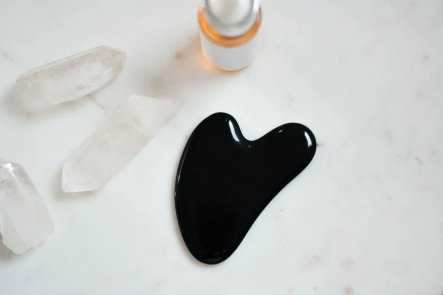 A black gua sha next to a face serum