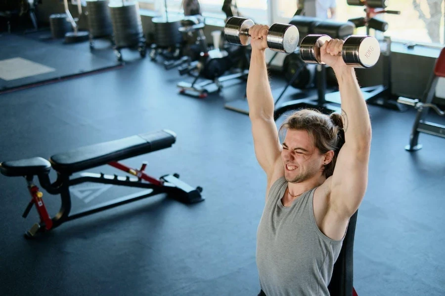 A man lifting dumbbells next to an adjustable bench