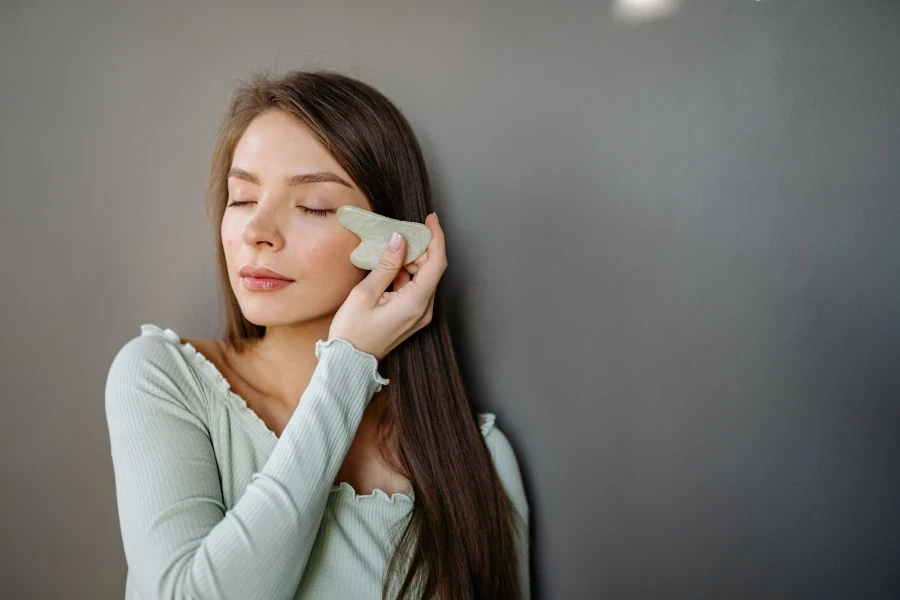 Uma mulher usando um gua sha nas maçãs do rosto