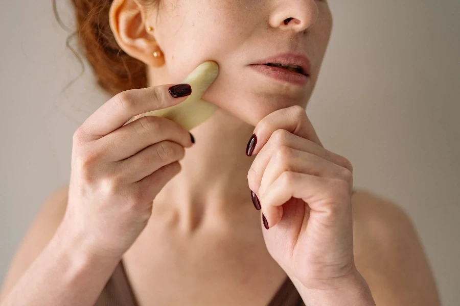 Una mujer usando un gua sha en su mandíbula.