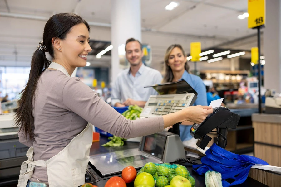 Pareja latinoamericana comprando en el supermercado y pagando con tarjeta al cajero