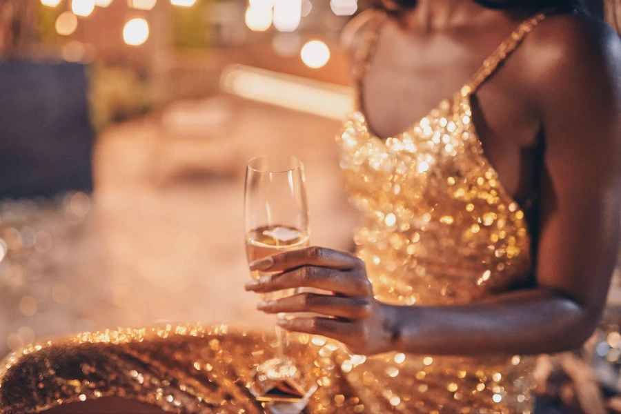 Gece elbisesi giymiş güzel genç Afrikalı kadın elinde şampanyayla flüt tutuyor.