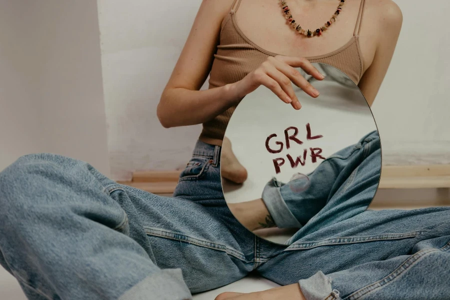 Woman in Brown Tank Top and Blue Denim Jeans Holding Round Mirror