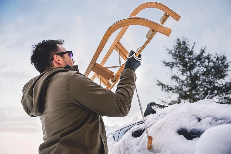 Uomo che indossa una giacca invernale grigia che mette la slitta sul tetto dell'auto