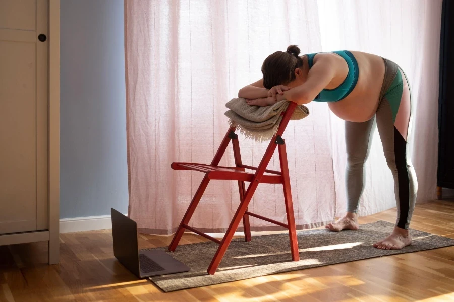 Schwangere Frau macht Yoga-Pose zu Hause mit Stuhl