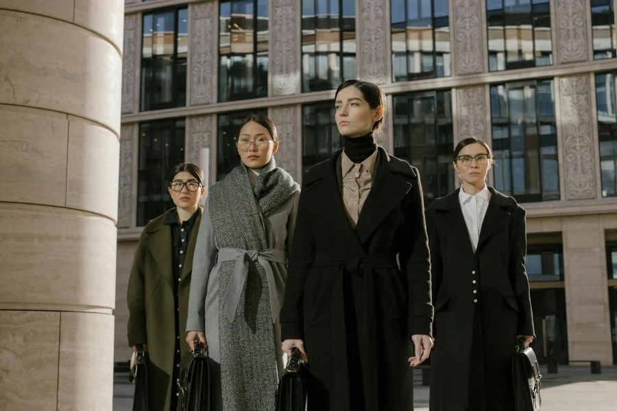 Frauen mit Brille stehen hinter einer Frau im schwarzen Mantel