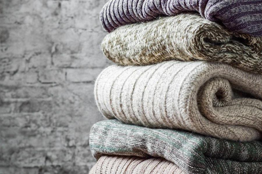 Stack of cozy knitted sweaters on gray wall background