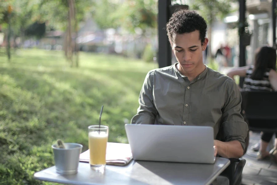 Libero professionista maschio nero concentrato che utilizza il computer portatile in un caffè di strada