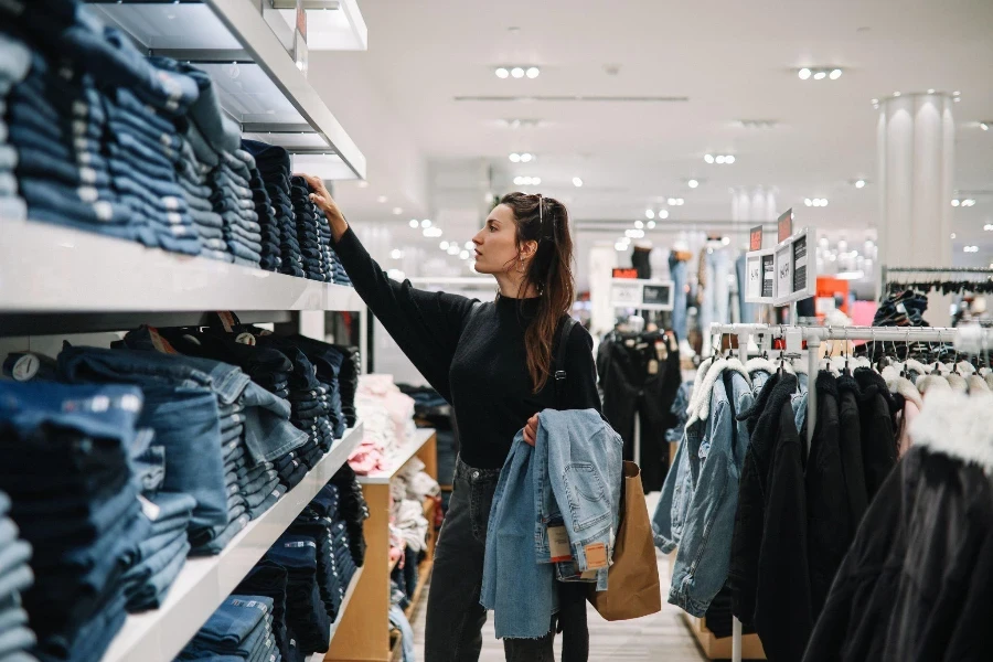 30'lu yaşların ortalarında bir kadın bir alışveriş merkezinde veya giyim mağazasında denim kot pantolon almaya gidiyor