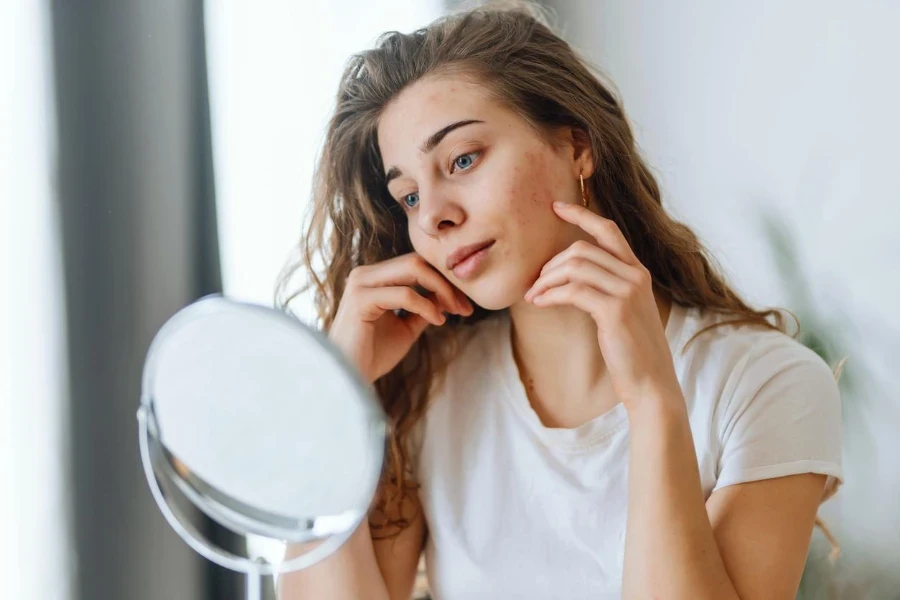 Giovane donna con pelle problematica che guarda nello specchio