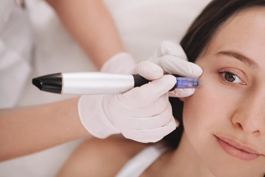 Foto seorang ahli kosmetologi profesional menggunakan dermapen pada klien wanitanya