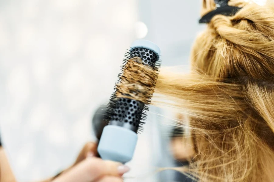 Wanita muda di salon rambut, penata rambut menggunakan sikat bouncing curl