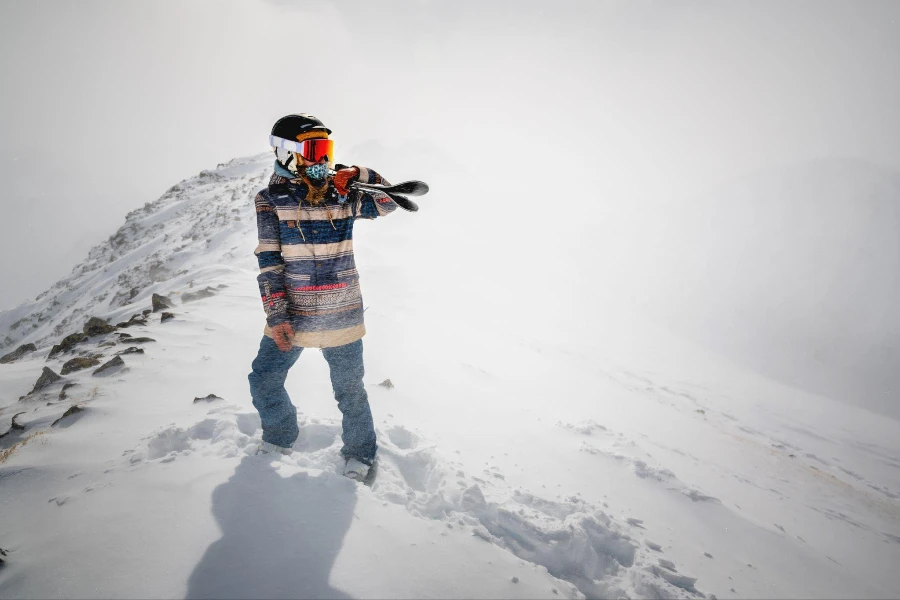 Foto lengkap seorang pemain ski ceria membawa alat skinya di bahunya