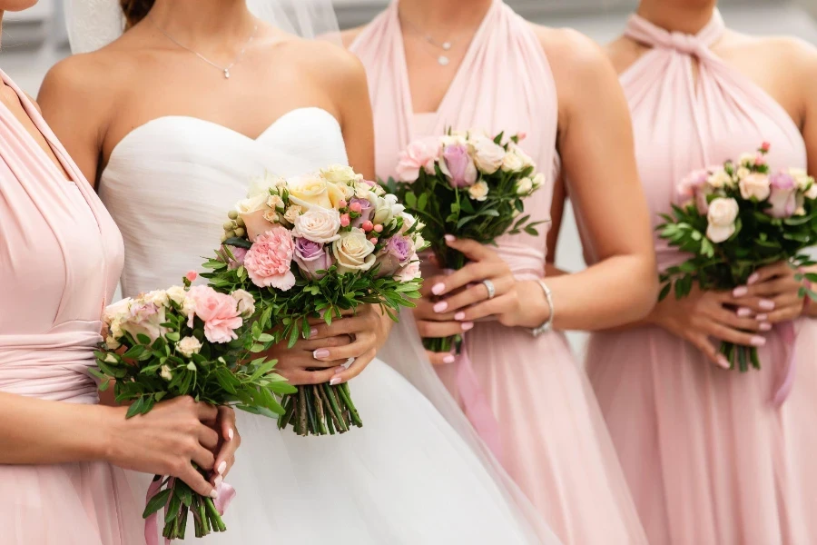 Braut und Brautjungfern in rosa Kleidern posieren mit Blumensträußen am Hochzeitstag