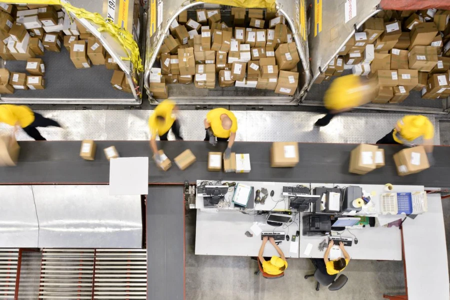 Trabajadores procesando cajas en cinta transportadora en almacén de distribución, movimiento borroso.