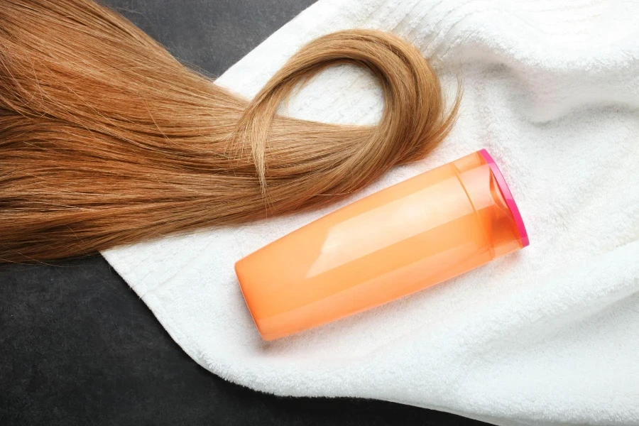 Cacho de cabelo feminino, shampoo e toalha turca em fundo preto