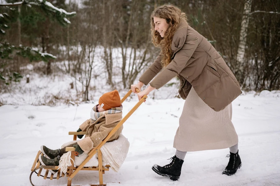Una donna che spinge il suo bambino su un passeggino a slitta in legno