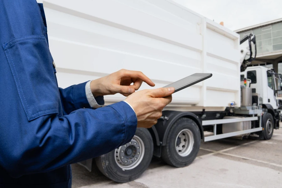 Manajer dengan tablet digital di samping truk sampah.