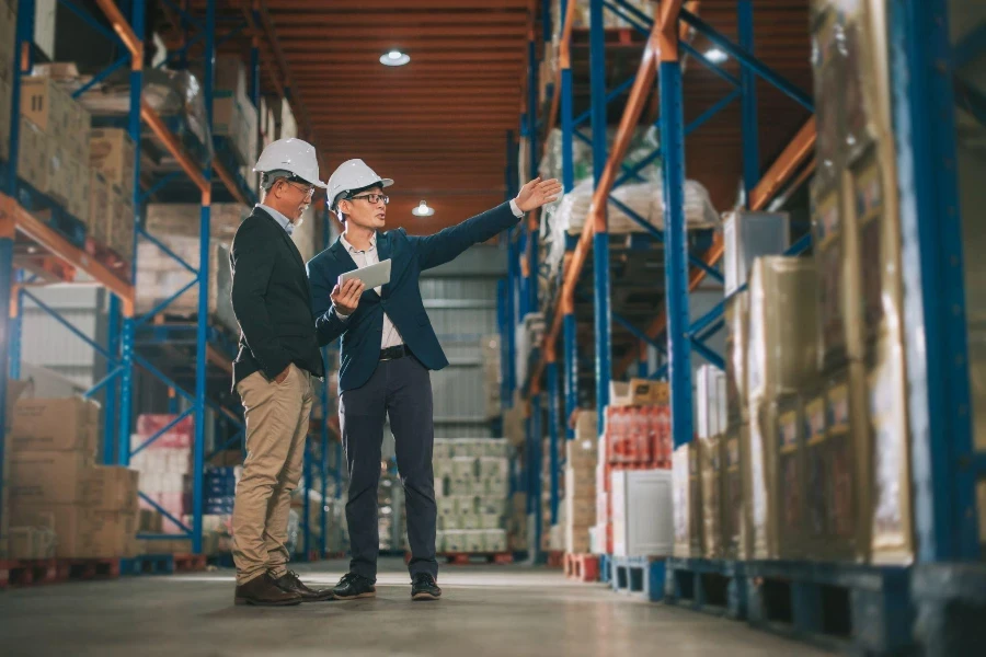 Asian Chinese management having discussion at warehouse with white hardhat using digital tablet