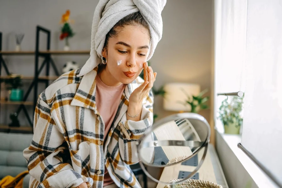 una bella giovane donna seduta in soggiorno applicando la crema per il viso