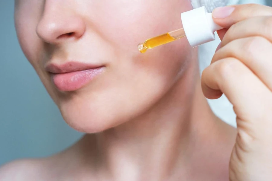 Weibliches Gesicht und Pipette mit Vitamin-C-Serum in Nahaufnahme auf grauem Hintergrund