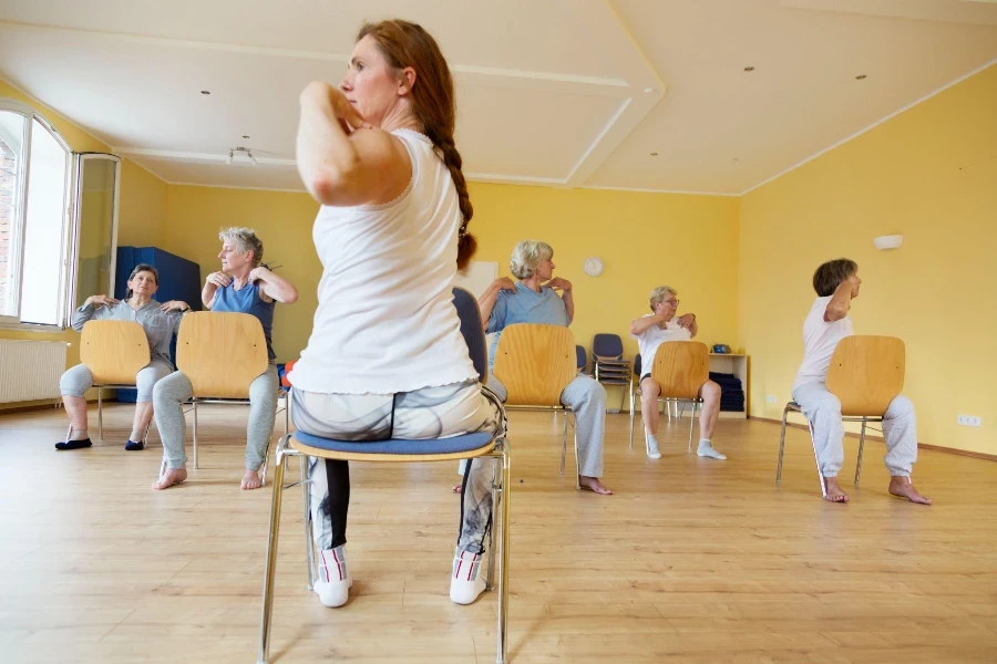 Profesora y clase de yoga para mujeres mayores activas en sillas en un estudio de yoga