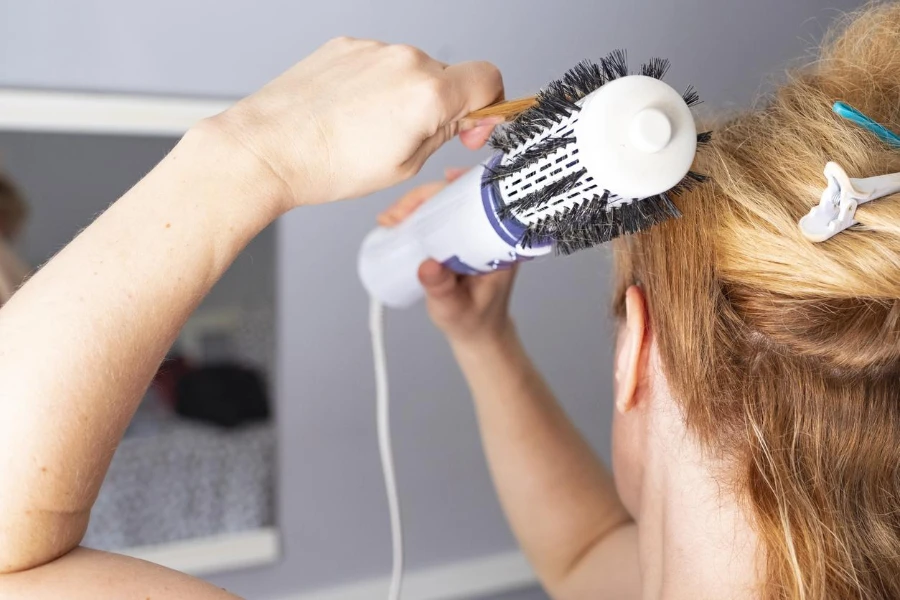 Mädchen glättet Haare mit einem Volumenbürsten-Bürstentrockner