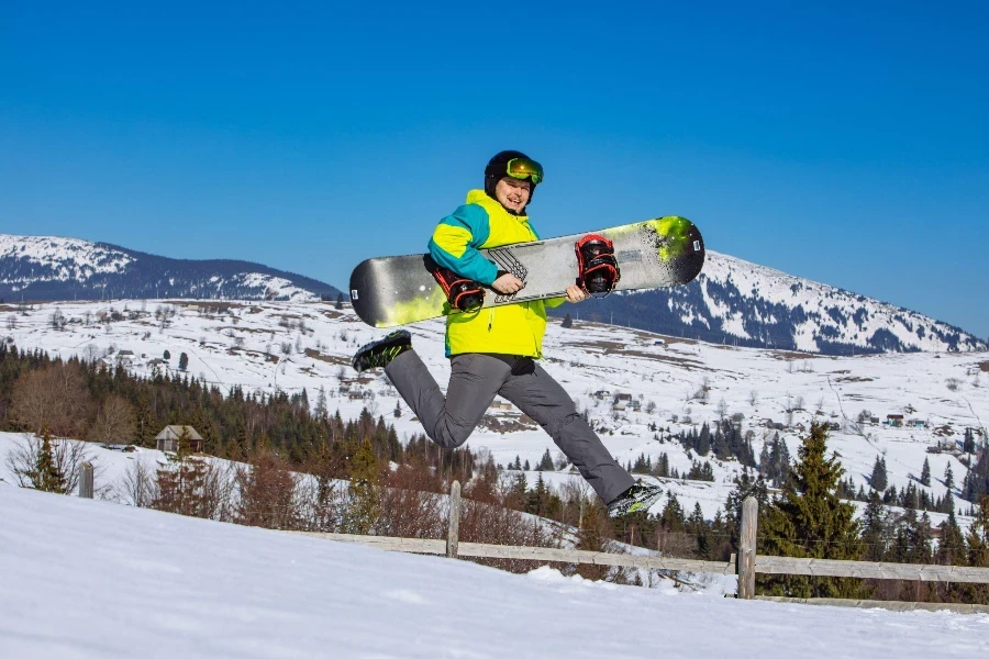 Elinde snowboard ile arka planda dağlarda zıplayan adam