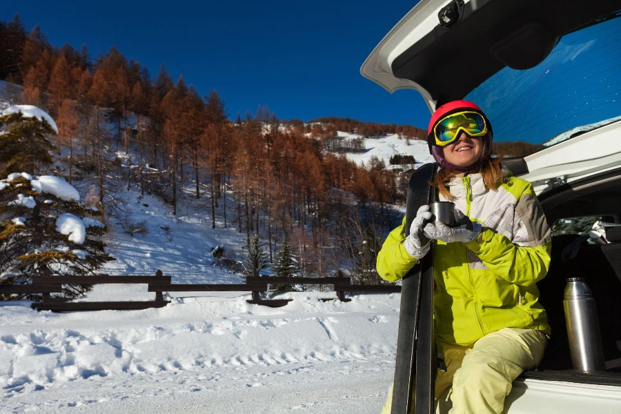 Glückliche junge Frau, die sich nach dem Skifahren im geöffneten Kofferraum ausruht